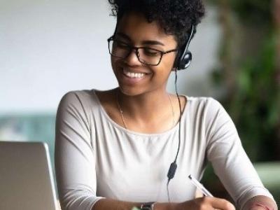 Woman smiles while writing and using laptop